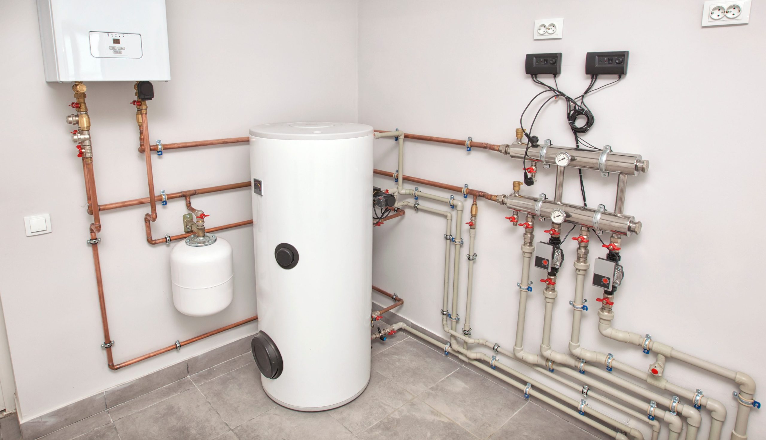 A modern heating system setup in a utility room with a white boiler, cylindrical water tank, pipes, valves, gauges, and electrical controls—ideal for monitoring boiler signs that may indicate the need for timely boiler repair. A modern heating system setup in a utility room with a white boiler, cylindrical water tank, pipes, valves, gauges, and electrical controls—ideal for monitoring boiler signs that may indicate the need for timely boiler repair.